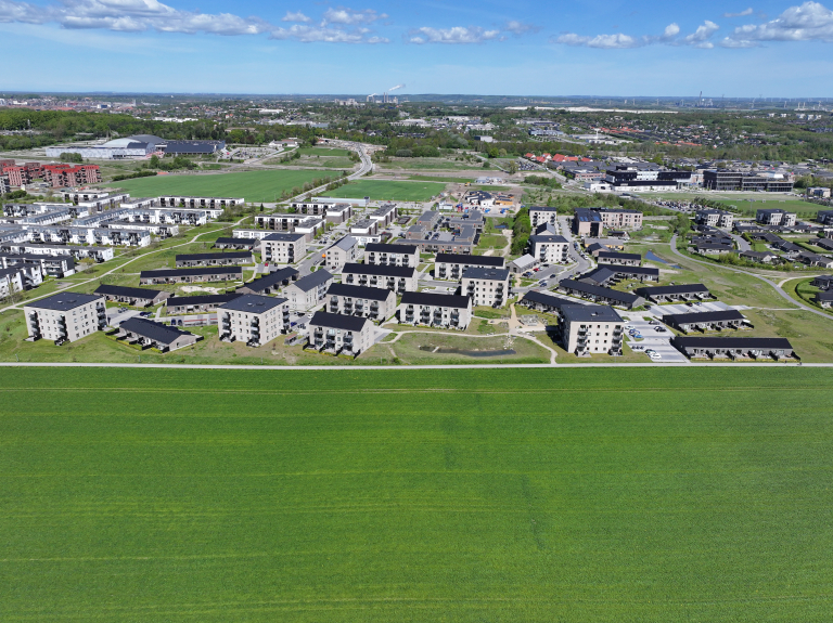 Luftfoto af et moderne boligområde med etageejendomme og rækkehuse op til en grøn mark